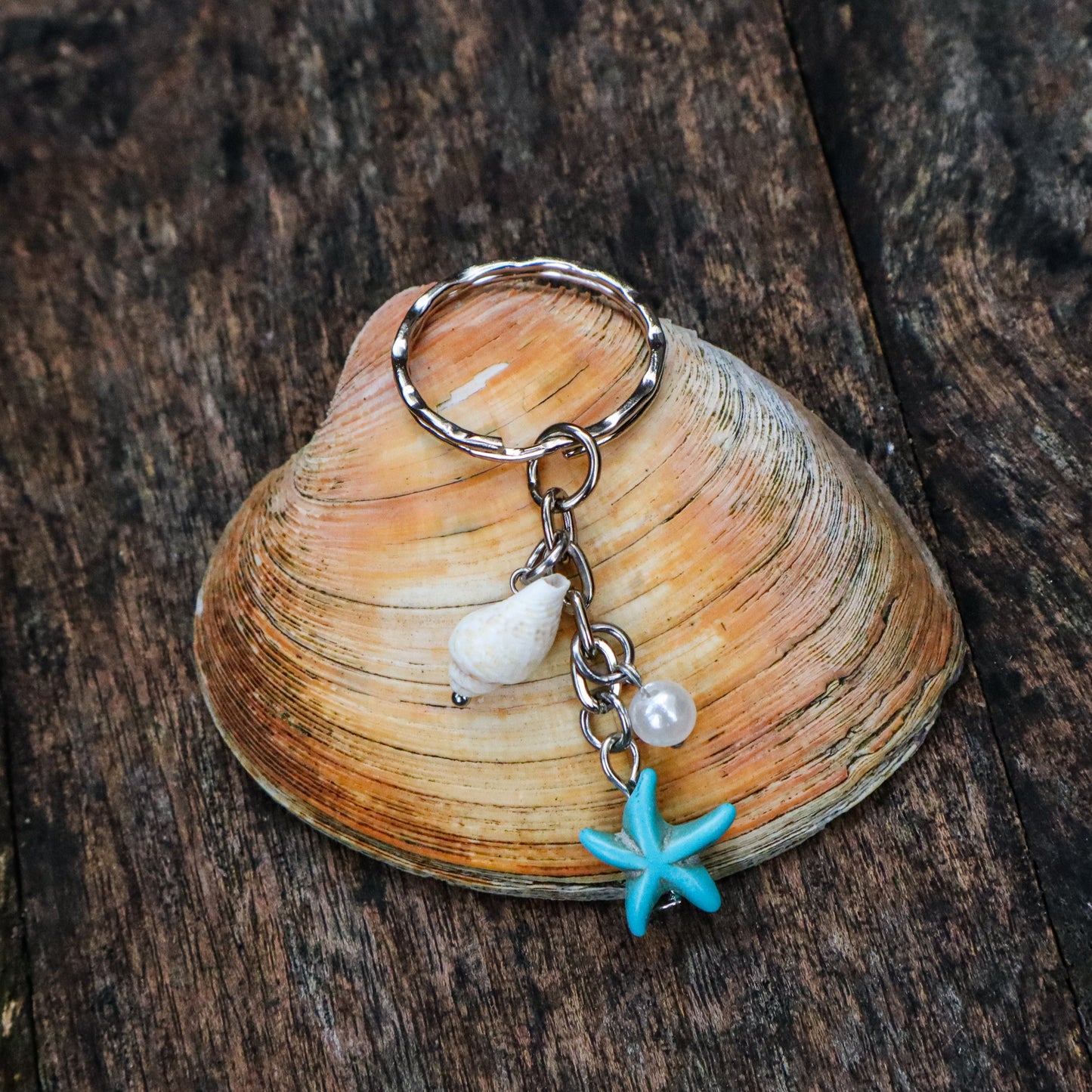 Keychain with starfish and shell charm on a seashell against a wooden background