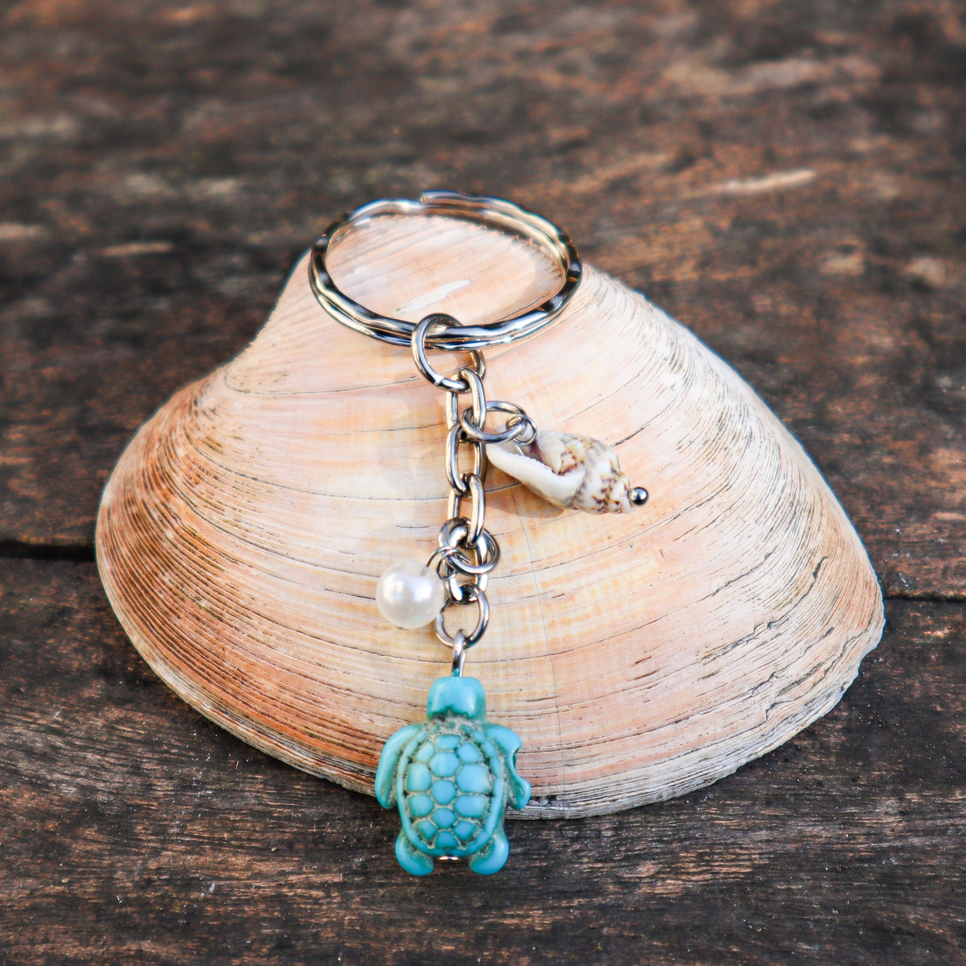 Keychain with turtle charm and pearl on a shell against a wooden background