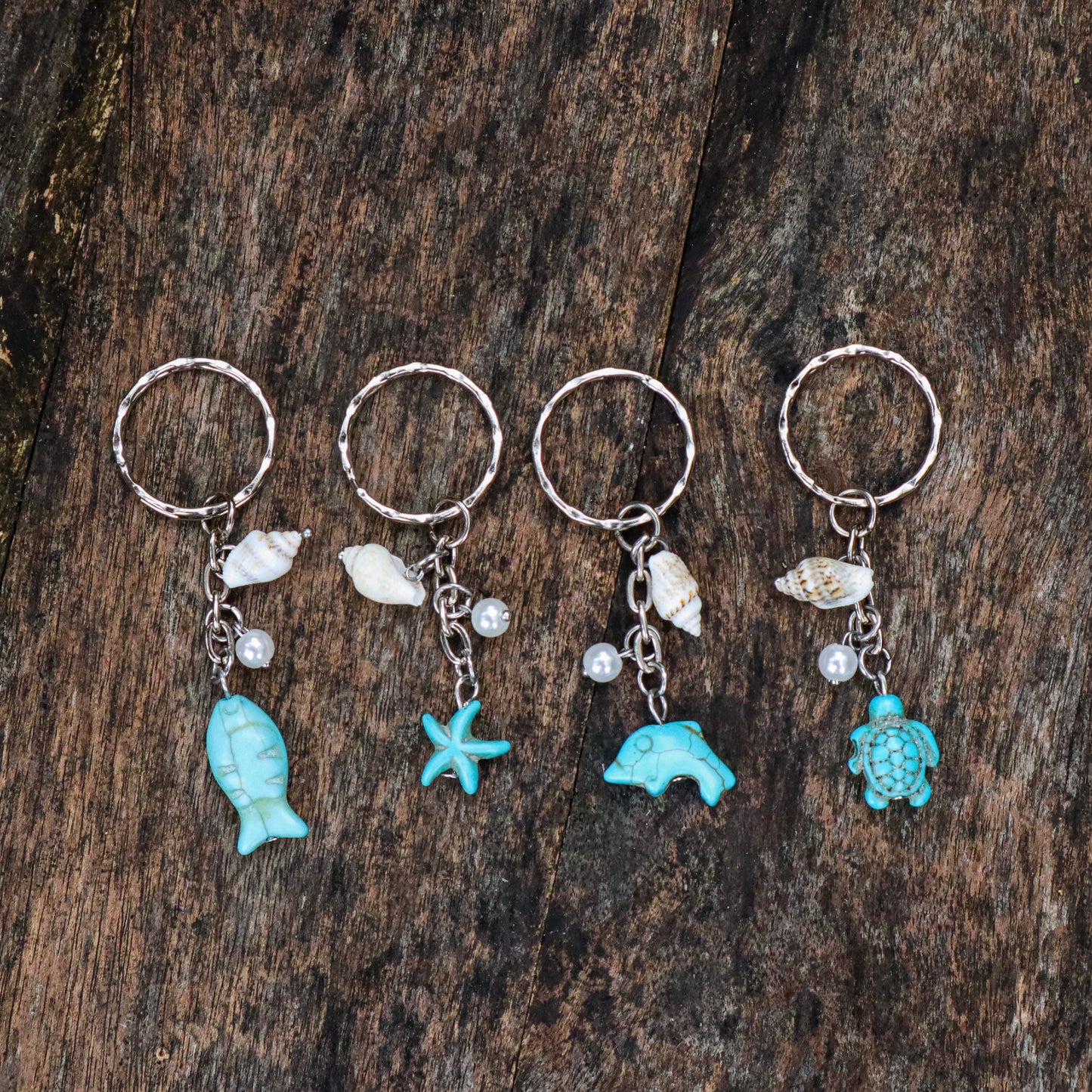 Four keychains with ocean-themed charms on a wooden surface