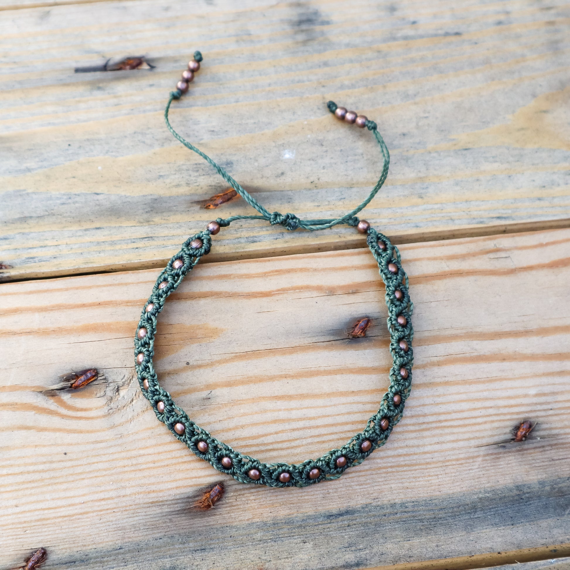 Green macrame ankle  bracelet with brown copper beads on a wooden surface