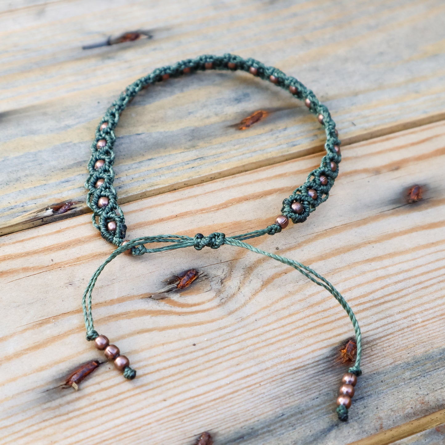 Green macrame ankle bracelet with copper beads on a wooden surface