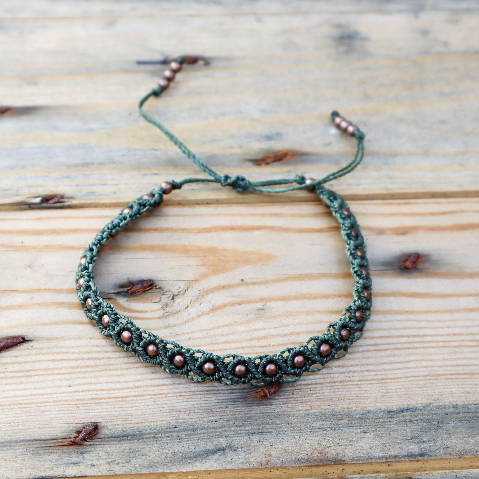 Green macrame  ankle bracelet with brown beads on a wooden surface