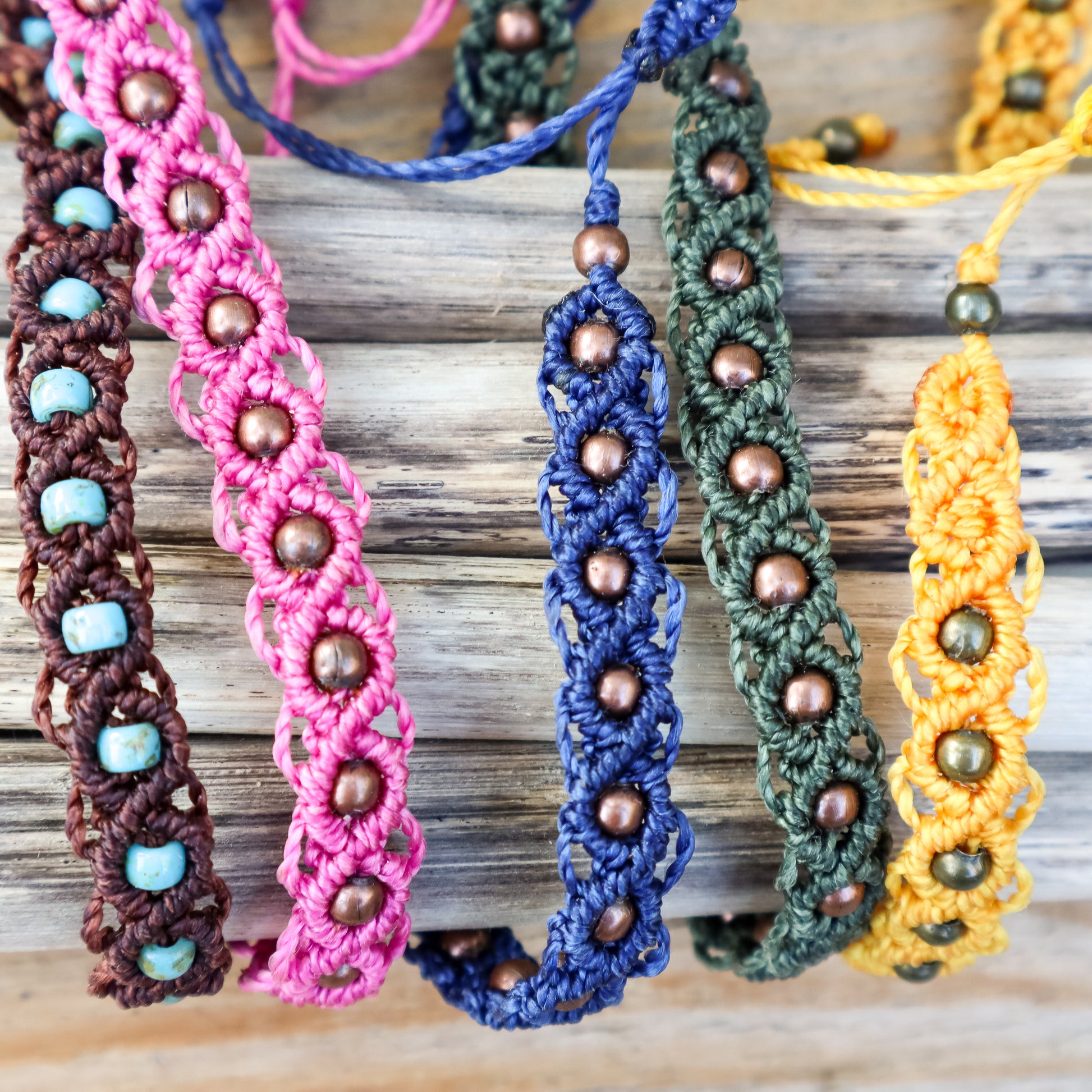 Colorful macrame ankle bracelets with beads on a wooden surface