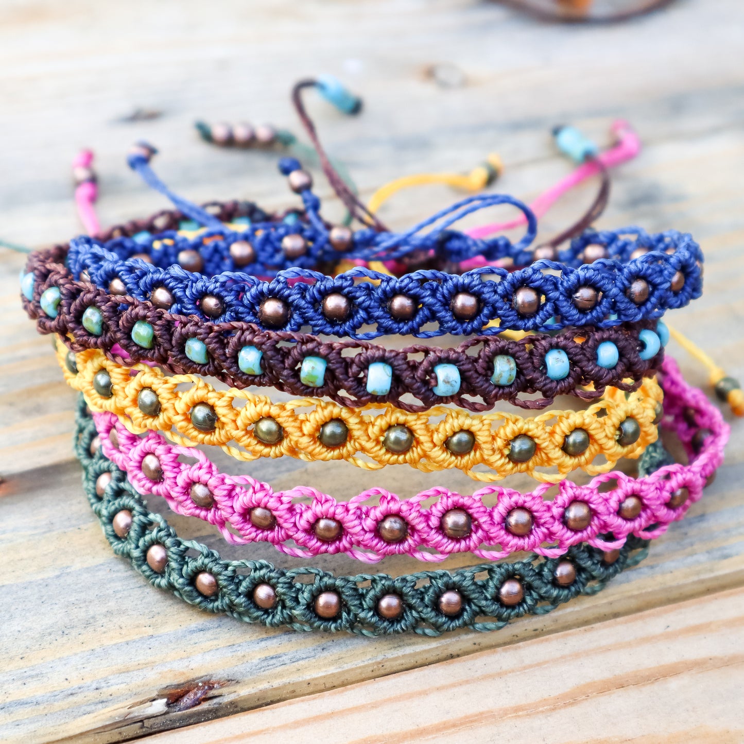 Stack of colorful macrame ankle bracelets on a wooden surface