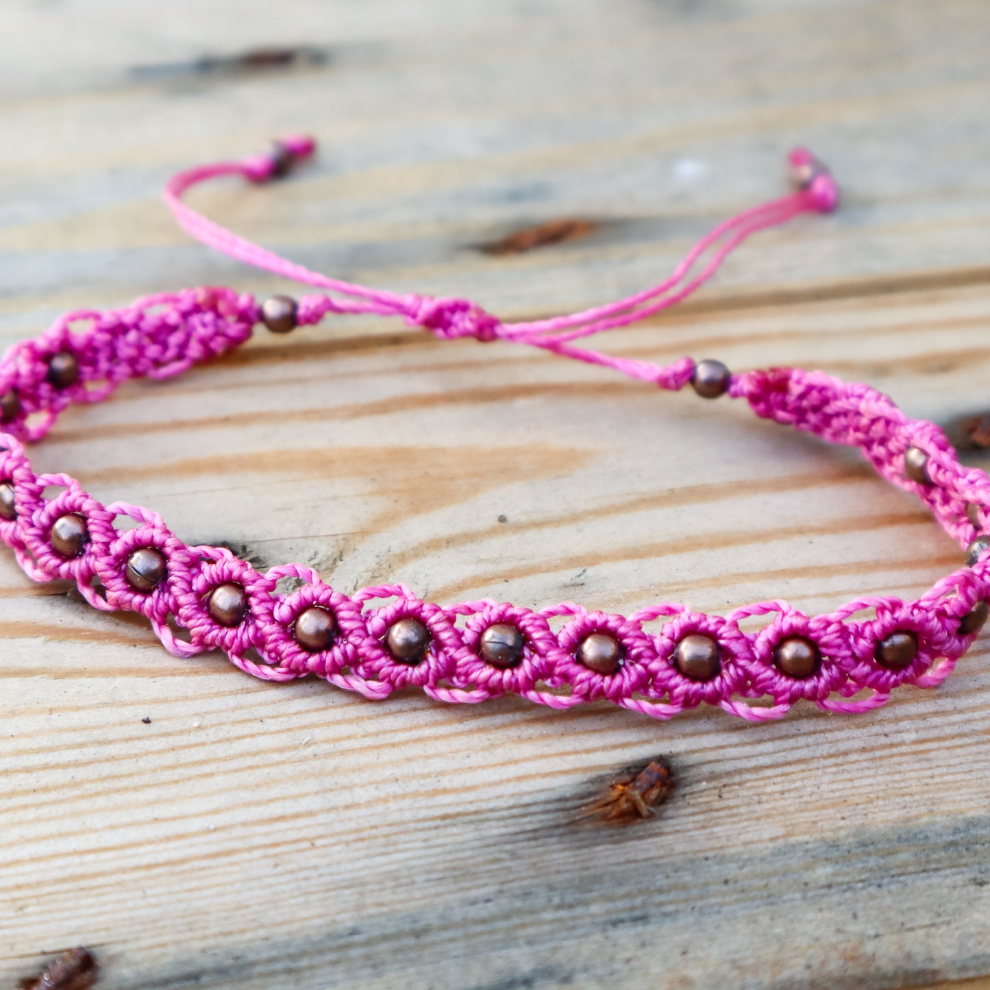 Pink macrame ankle bracelet with bronze beads on a wooden surface