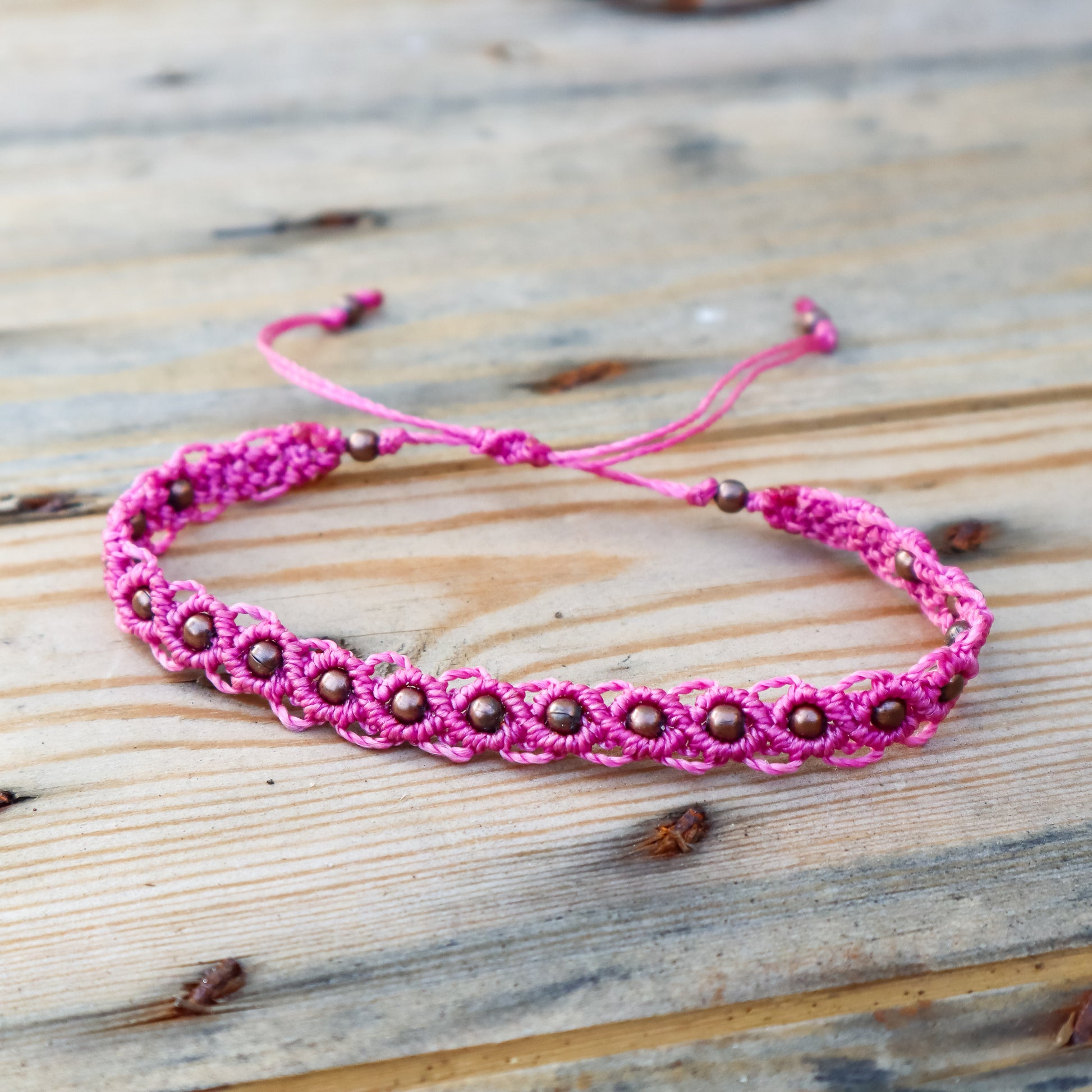 Pink macrame ankle bracelet with bronze beads on a wooden surface
