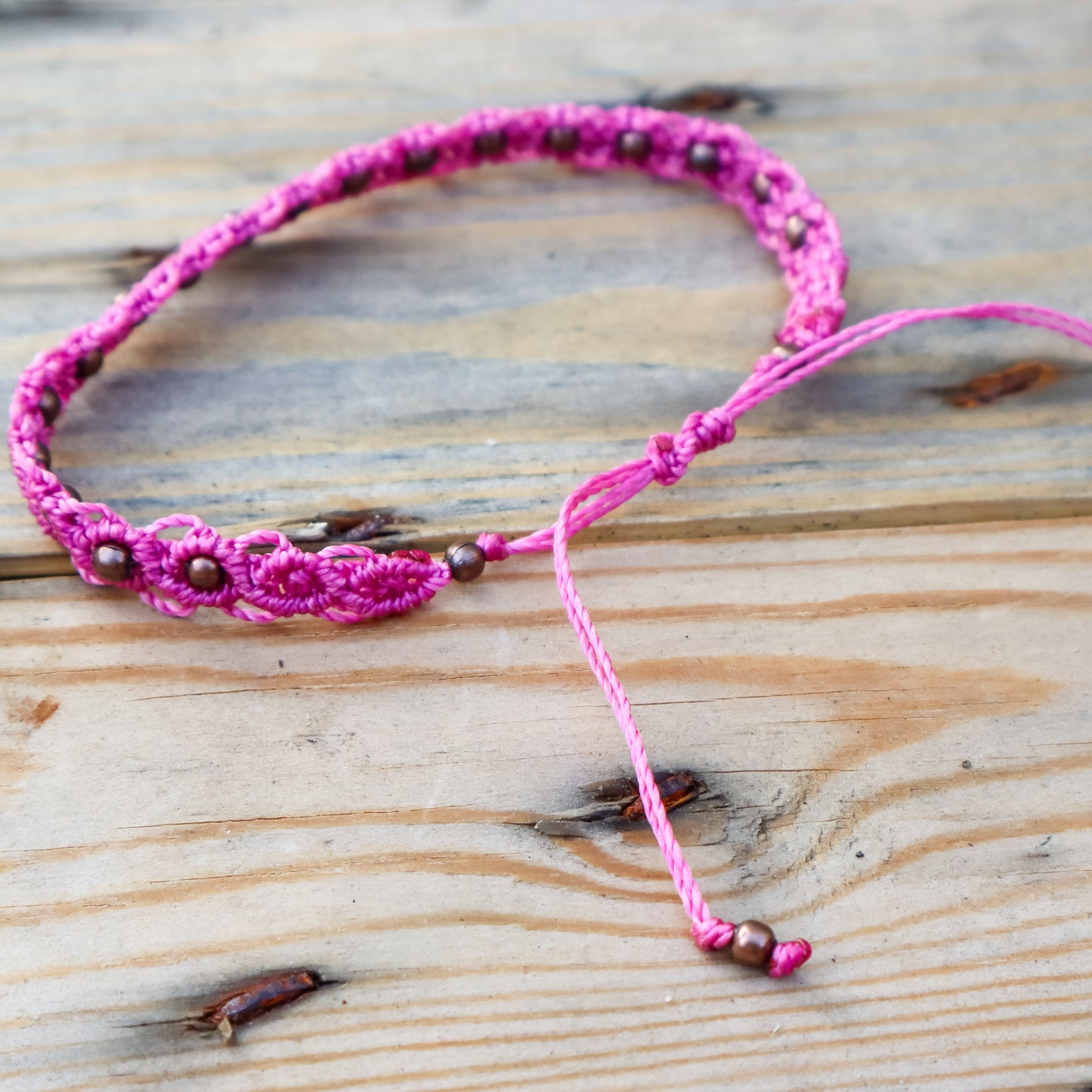 Pink macrame ankle bracelet with bronze beads on a wooden surface