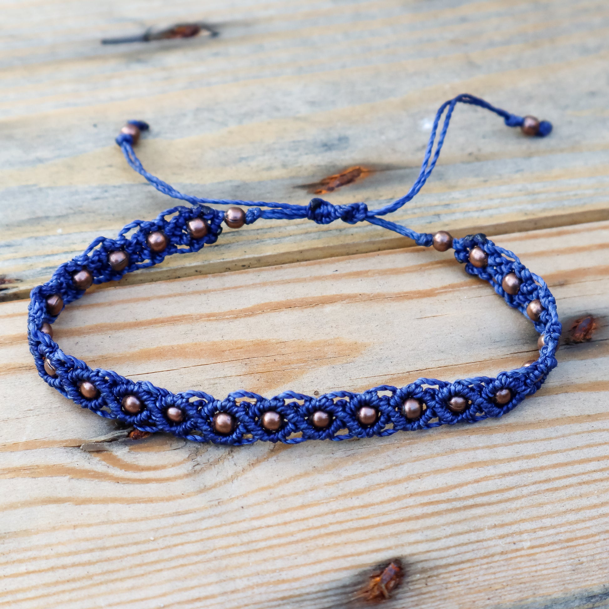 Blue braided bracelet with copper beads on a wooden surface