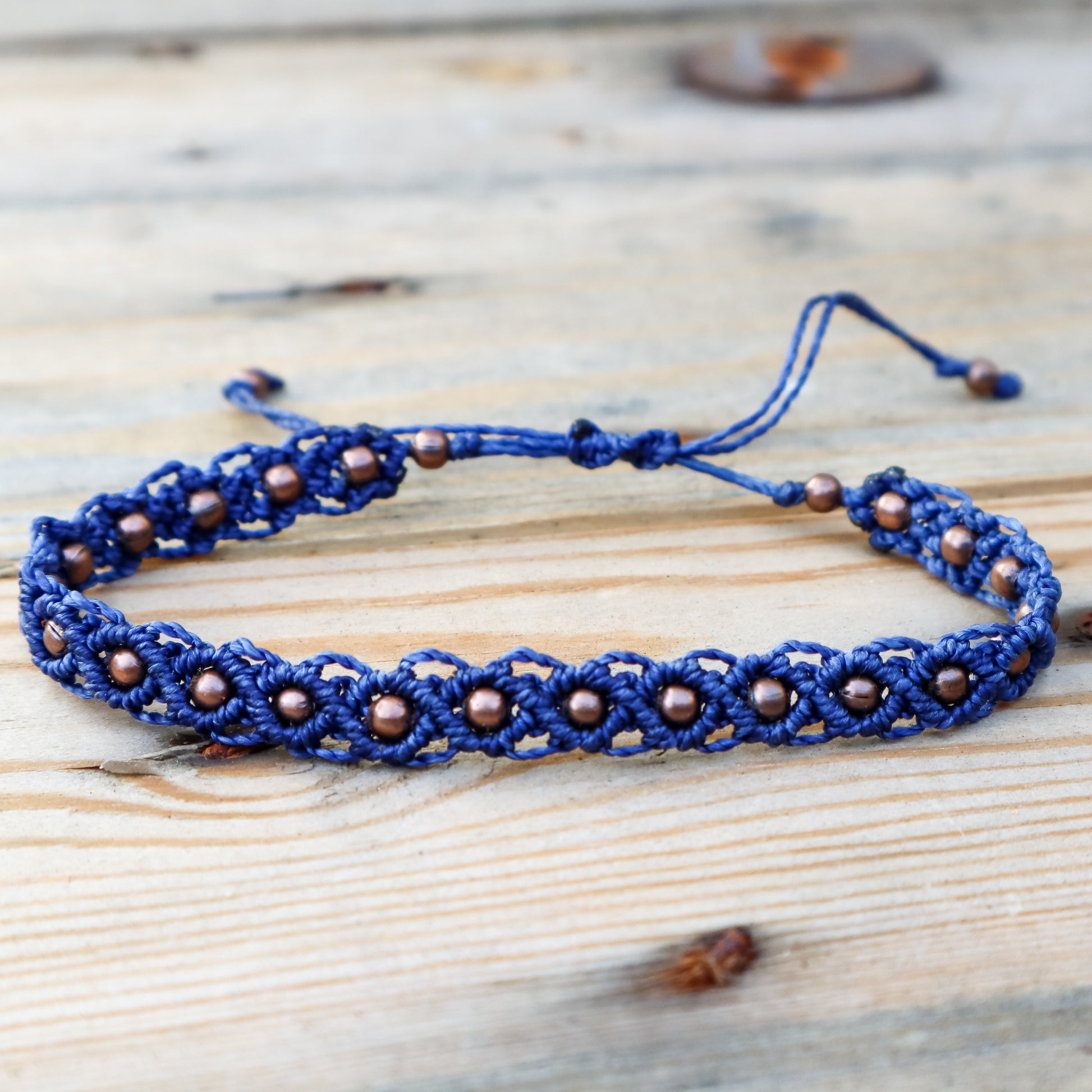 Blue macrame bracelet with copper beads on a wooden surface