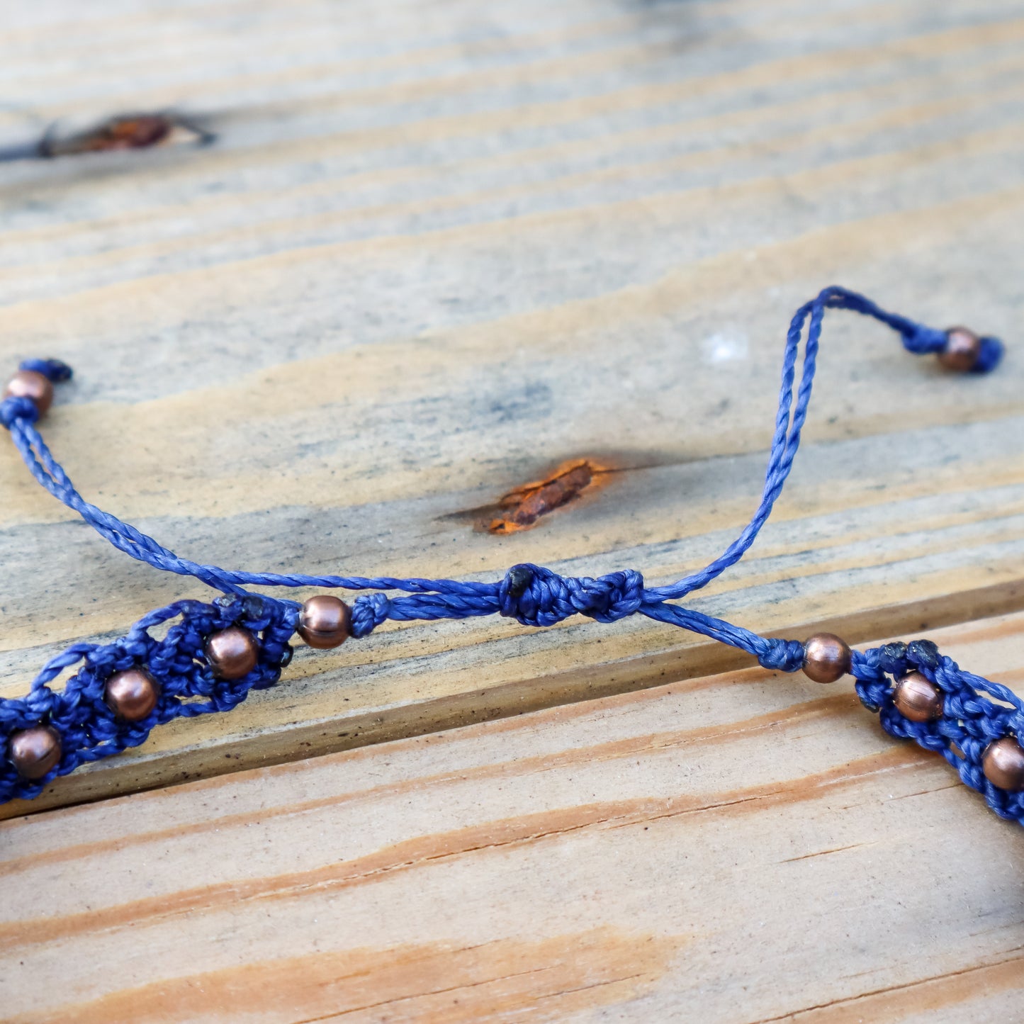 Close up of a blue macrame ankle bracelet with copper beads on a wooden surface