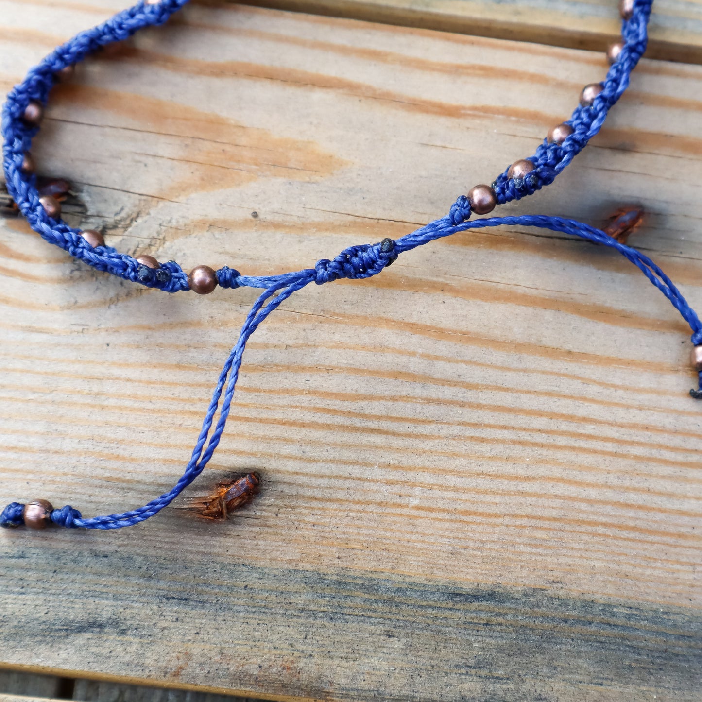Blue macrame bracelet with copper beads on a wooden surface. Close up of the sliding knot closure