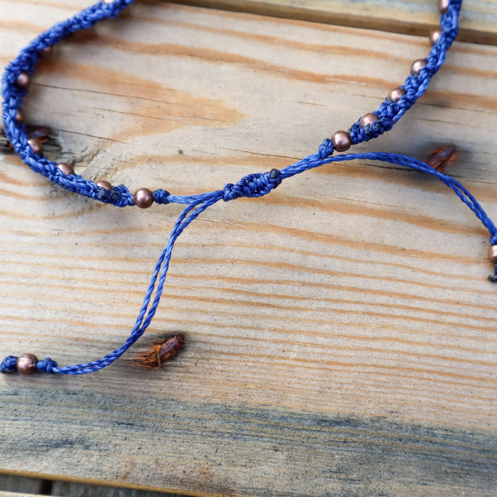 Blue macrame bracelet with copper beads on a wooden surface. Close up of the sliding knot closure