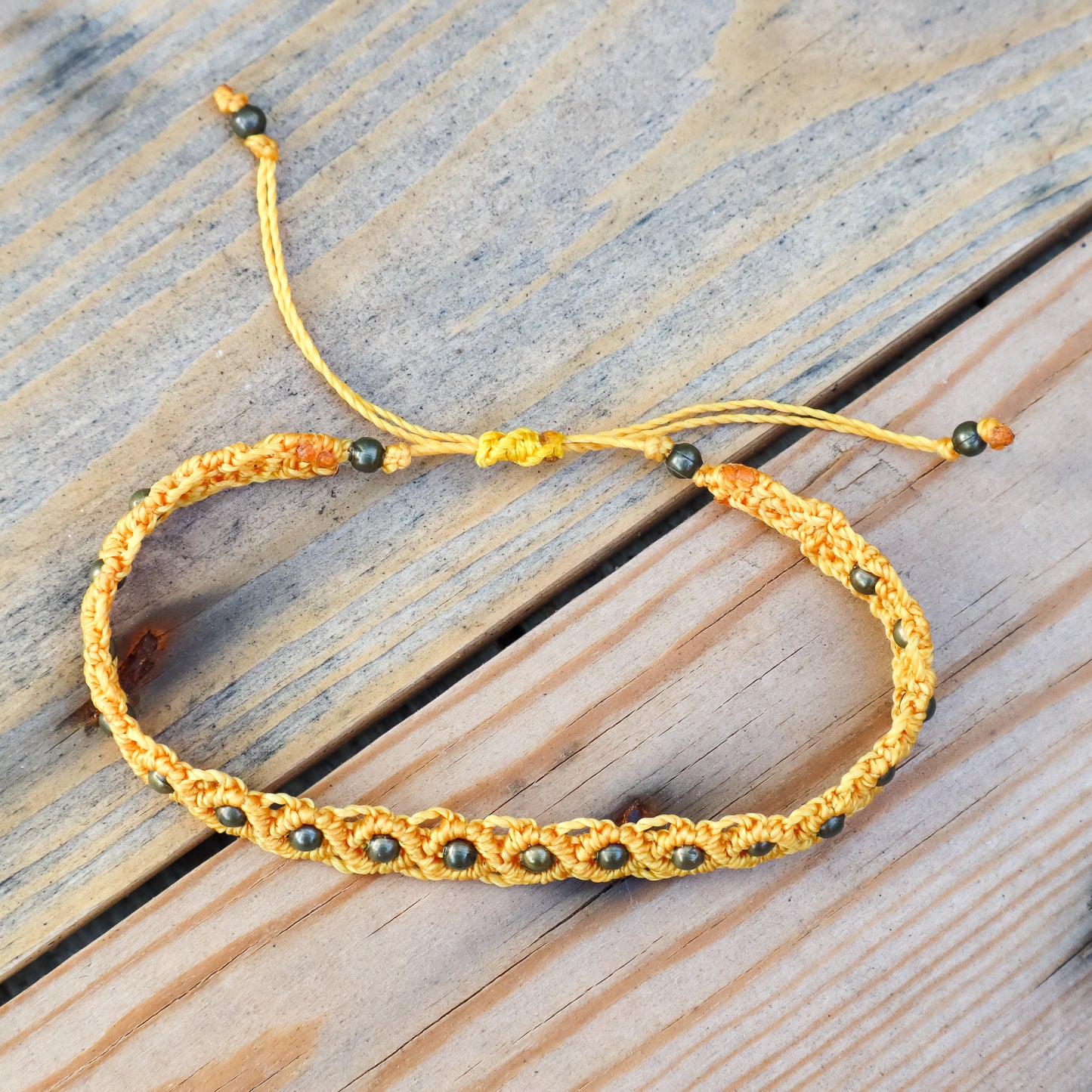 Yellow macrame ankle bracelet with bronze beads on a wooden surface