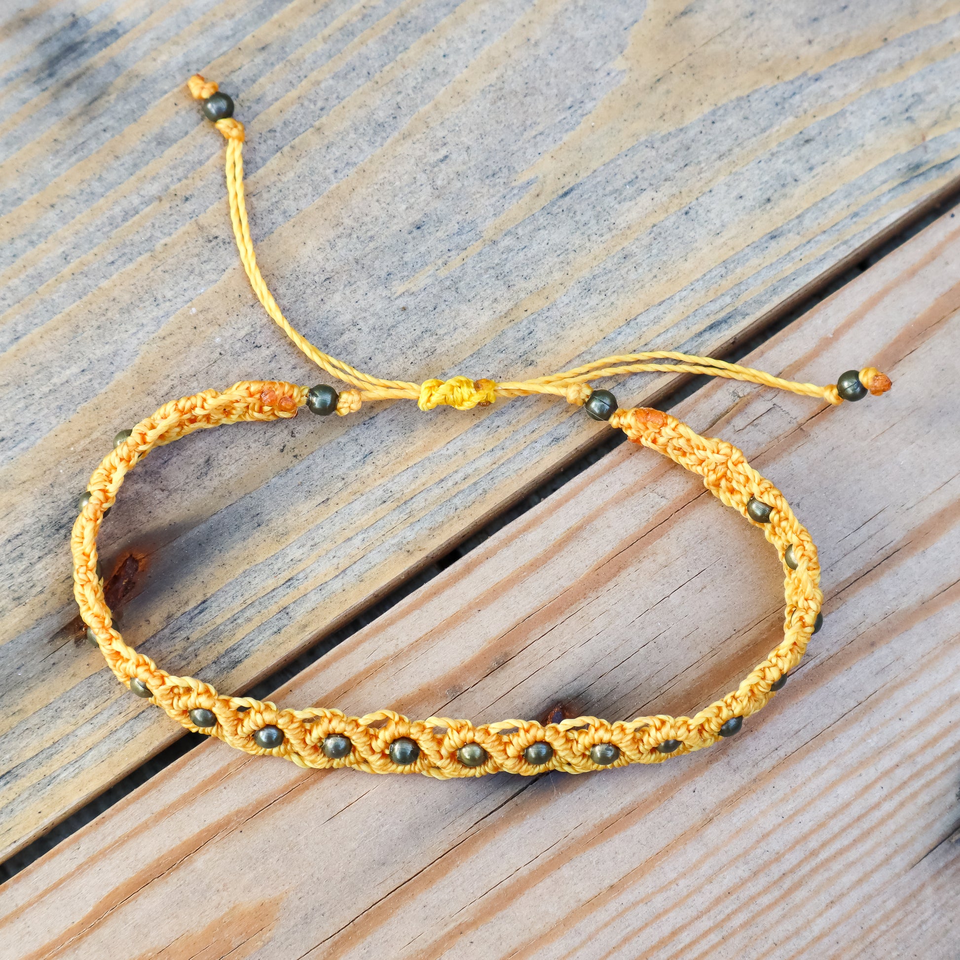 Yellow macrame ankle bracelet with bronze beads on a wooden surface