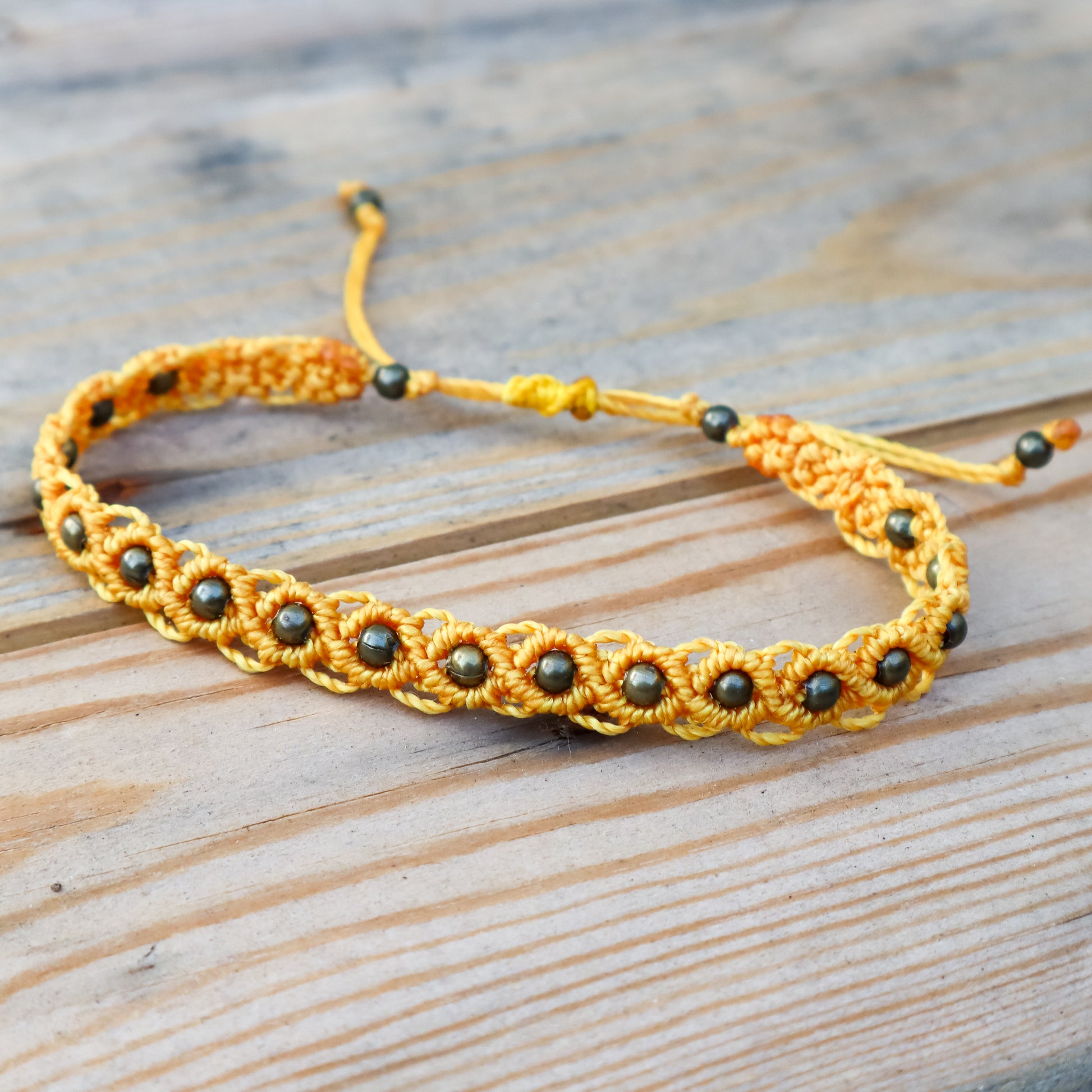 Yellow macrame ankle  bracelet with bronze beads on a wooden surface