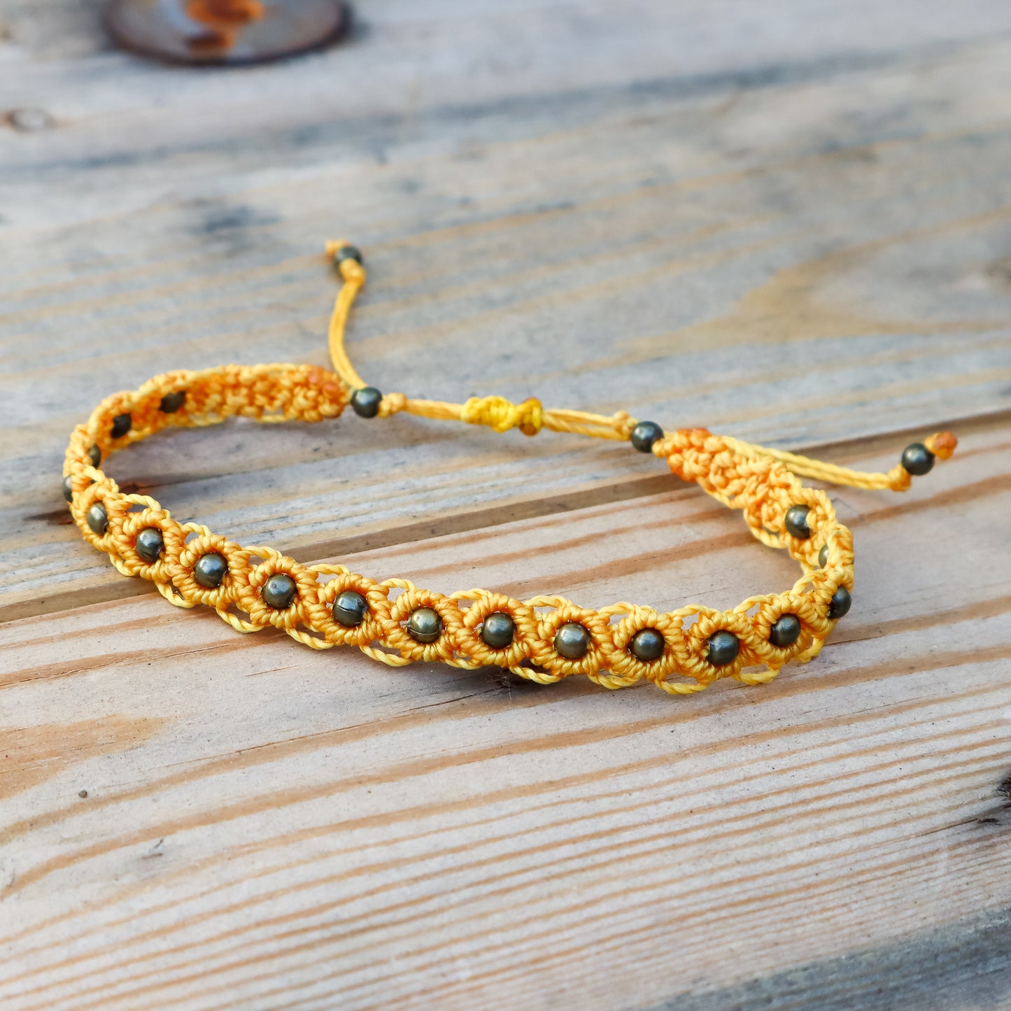 Yellow macrame ankle bracelet with bronze beads on a wooden surface