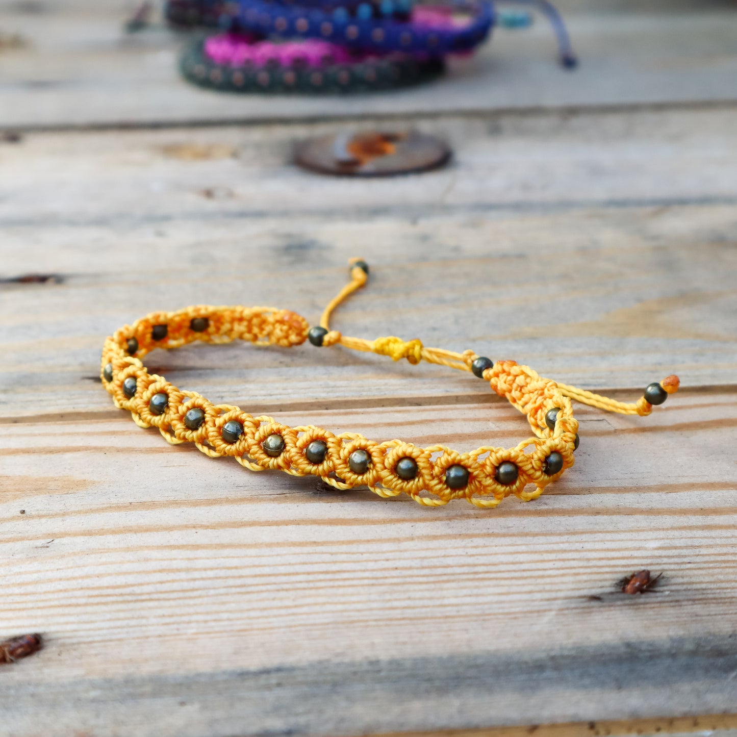 Yellow macrame ankle bracelet with bronze beads on a wooden surface