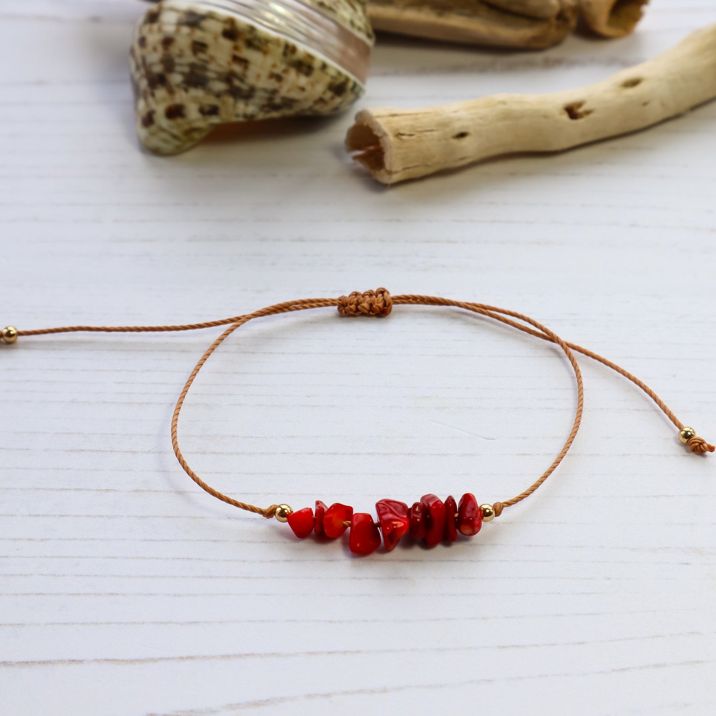 bracelet with red beads on brown cord on white wooden background with shells and wood in the background