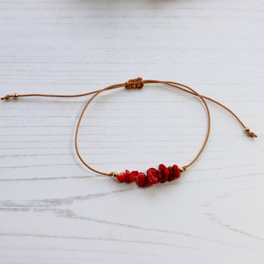 Bracelet with red crystals and brown cord on white wooden background